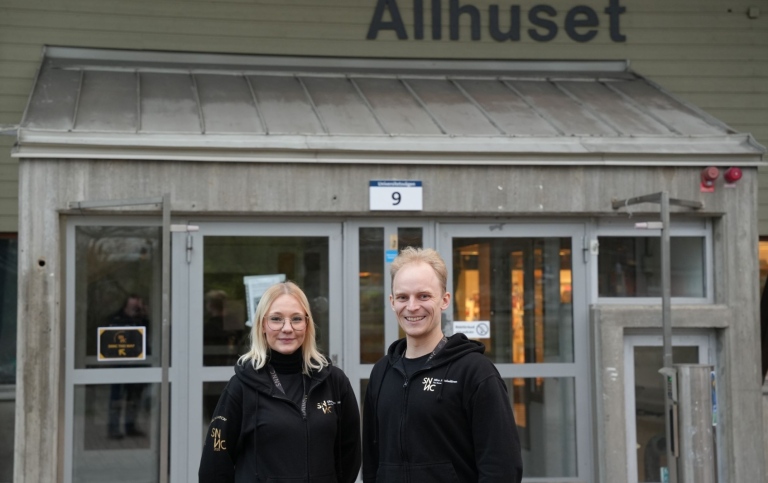 Olivae Odenskiöld och Miro Jääskeläinen i arbetskläder framför entrén till Allhuset